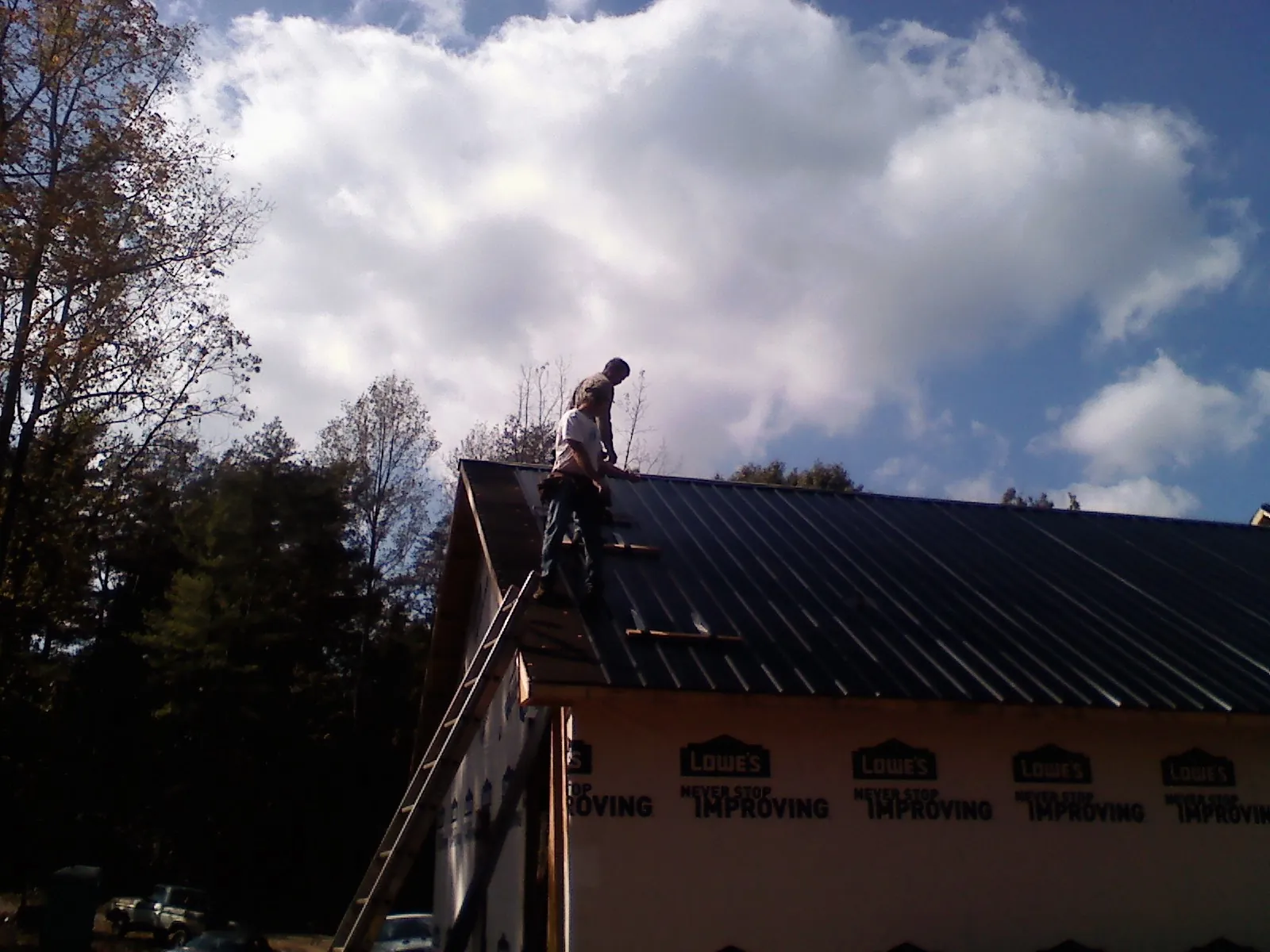 Roofer fastening dark metal panels high against a cloudy sky, from a Roof Inspection job in Dunbar